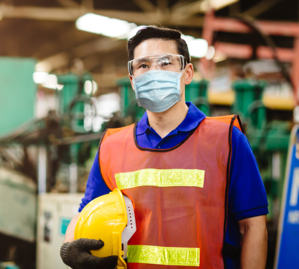 Man wearing a face mask and orange vest and carrying a hardhat