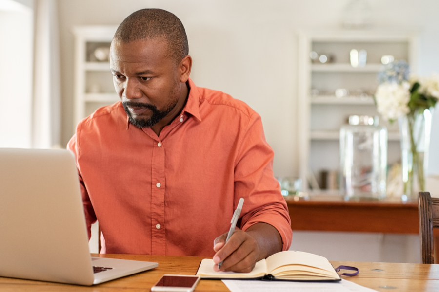 Man in orange shirt looking at laptop.