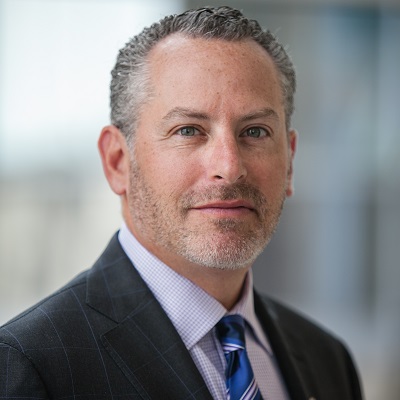 Tobi Millrood in a dark suit with blue pattern tie