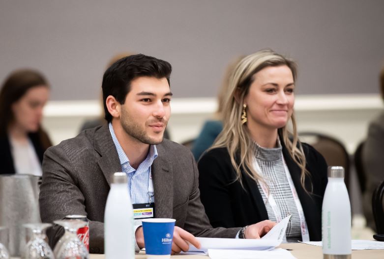 A man and a woman sitting next to each other in a meeting smiling.
