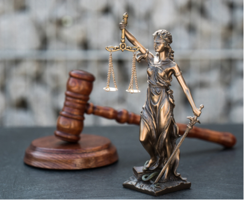 Wooden gavel with a metal lady justice statute on a table.