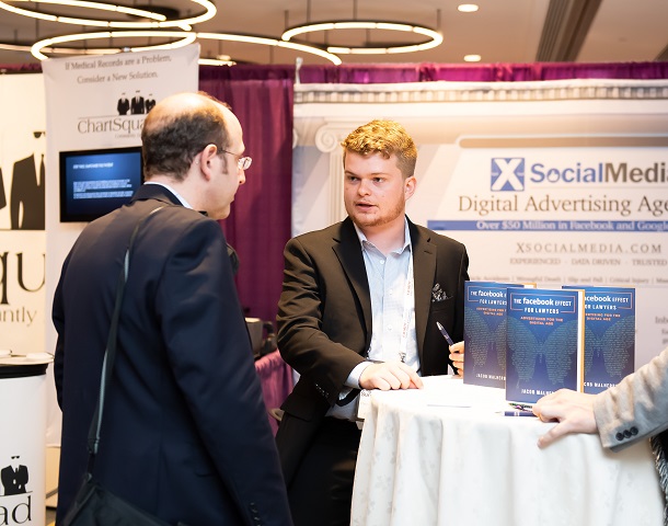 Two men talking in front of a booth at a convention.