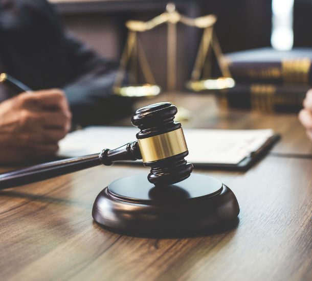 A photo of a gavel on a table with the scale of justice in the background