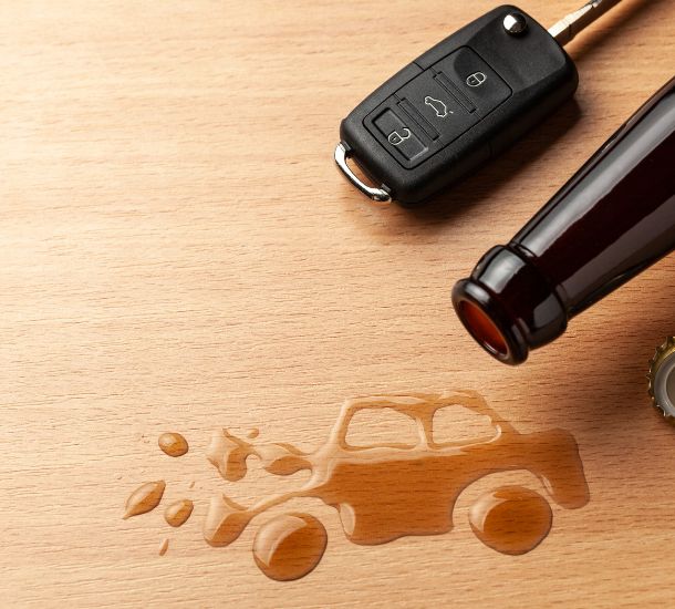 A close up photo of the neck of a beer bottle, car keys, and beer liquid that has been edited in the shape of a car